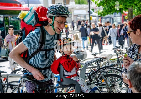 Ein junger Vater mit seinem Kind Sohn glücklich und lächeln sehen, wie Sie mit ein paar Damen sprechen, tragen Fahrradhelme bereit zum Zyklus entfernt. Stockfoto