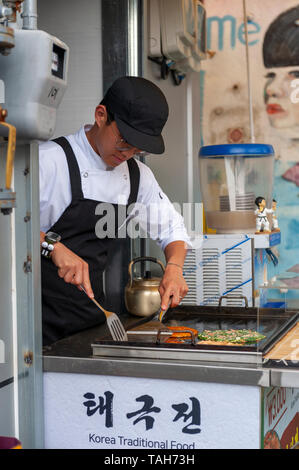 Junger Mann Anbieter kochen Pfannkuchen Buchimgae oder Koreanisch, Koreanisch traditionelles Essen, an einer Garküche in Gamcheon Culture Village in Busan, Südkorea Stockfoto