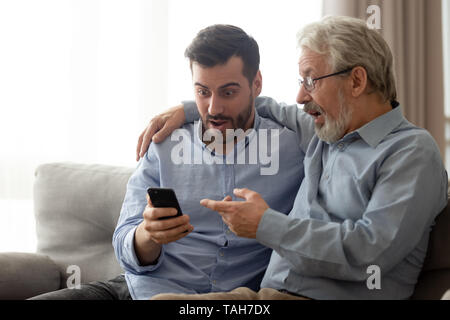 Junger Mann mit älteren Vater schockiert das Lesen von Nachrichten auf dem Smartphone Stockfoto