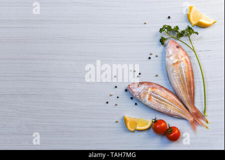 Frischen, rohen Fisch und Meeresfrüchte mit Kräutern und Gewürzen mit Zitrone Petersilie Tomaten Pfeffer Saatgut auf weißem Holz Hintergrund Stockfoto