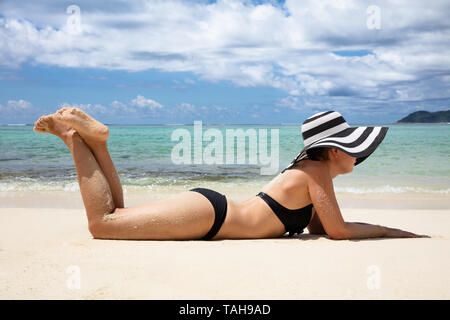 Seitenansicht einer jungen Frau im Bikini liegt am Strand in der Nähe des Meeres Stockfoto