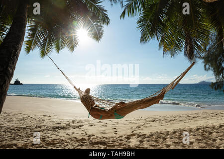 Liegende Frau auf der Hängematte zwischen den Palmen Vor Meer am Strand Stockfoto