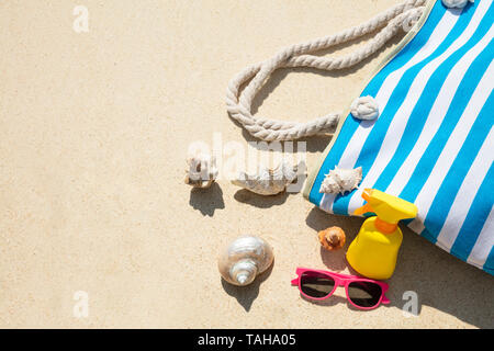 Seashells, Sonnenbrille, Sonnencreme Flasche und Handtasche auf Sand am Strand Stockfoto