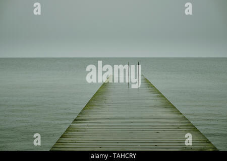 Eine leere Nass stabrost Pier/Pontoon und Badeleiter führenden heraus zum Meer auf einem nassen grauen bewölkten Tag. Stockfoto