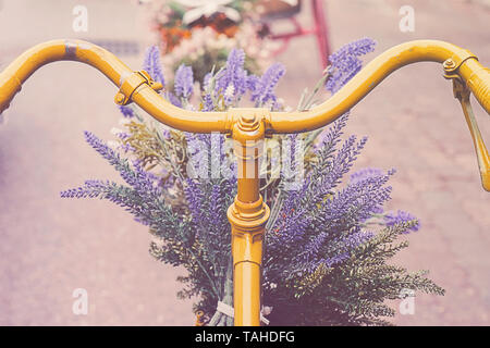 Rusty vintage Yellow Bike mit Korb mit Blumen gegen blured Hintergrund Stockfoto