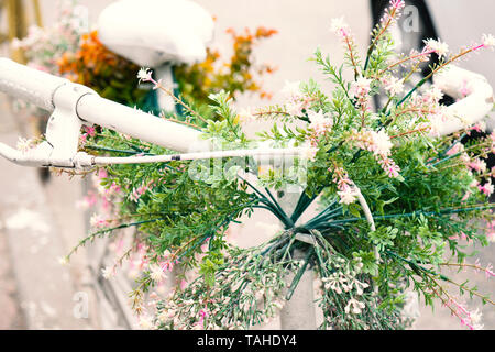Rusty Vintage White Fahrrad mit Korb mit Blumen gegen blured Hintergrund Stockfoto