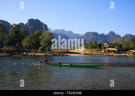 VANG VIENG, LAOS - Dezember 22. 2017: Blick über den Fluss auf Dorf von Karst Hügel Landschaft entlang (xong) Nam Song Fluss umgeben Stockfoto