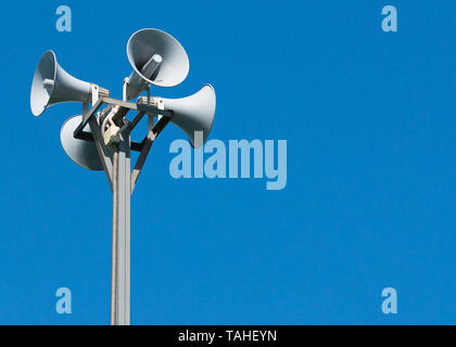 Eine große Säule mit vier grauen Lautsprecher in einem Kreis gegen einen sauberen blauen Himmel. Warnblinkanlage. Die Möglichkeit der Platzierung ihrer Test- oder Bild. Stockfoto