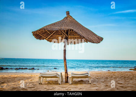 Paar Liege mit Sonnenschirm auf schöne leere Strand in der Nähe des Meeres. Es ist ein tropisches Paradies in Afrika, Senegal. Es ist blauer Himmel. Es ist die rechte Stockfoto