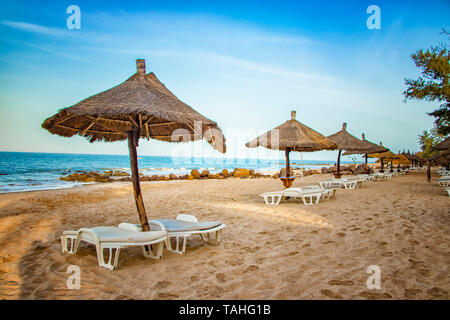 Paar Liege mit Sonnenschirm auf schöne leere Strand in der Nähe des Meeres. Es ist ein tropisches Paradies in Afrika, Senegal. Es ist blauer Himmel. Es ist die rechte Stockfoto