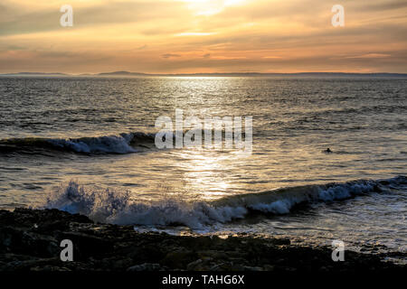 Drei Surfer genießen Sie den Sonnenuntergang bei der thet Warten awave, Rest Bay Porthcawl, Großbritannien. Stockfoto