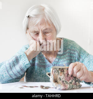 Betroffene ältere Frau am Tisch sitzen zählen Geld in Ihrem Portemonnaie. Stockfoto