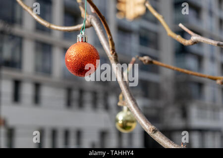 Ein funkelndes Rot, eher traurig, Christbaumschmuck, hängen von einer Niederlassung eines blattlosen Baum in Midtown Manhattan Stockfoto