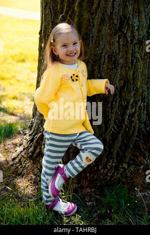 Kleines Mädchen lehnte sich lachend gegen einen Baumstamm, Tschechische Republik Stockfoto