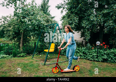 Junge schöne Hübsche kaukasische Mädchen Frau Spaß, lächelnd und Reiten Kick Scooter Stockfoto