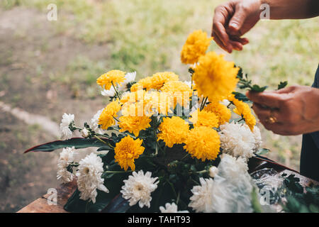 Florist Hände einen Blumenstrauß aus gelben und weißen Chrysantheme auf einem Holztisch. Selektive konzentrieren. Kopieren Sie Platz. Stockfoto