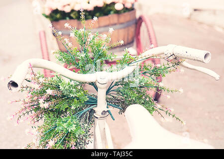 Rusty Vintage White Fahrrad mit Korb mit Blumen gegen blured Hintergrund Stockfoto