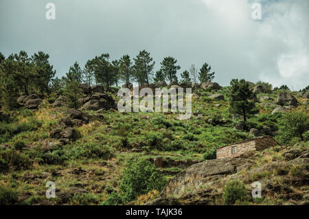 Rustikales Steinhaus auf einem hügeligen Landschaft mit Felsen und Büsche, in einem bewölkten Tag, in der Nähe von Villa Covelo. Wie die Portugiesische Schweiz für ihre Landschaft bekannt. Stockfoto