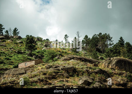 Rustikales Steinhaus auf einem hügeligen Landschaft mit Felsen und Büsche, in einem bewölkten Tag, in der Nähe von Villa Covelo. Wie die Portugiesische Schweiz für ihre Landschaft bekannt. Stockfoto
