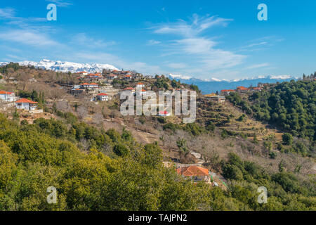 Panoramablick auf kleinen Bergstadt in der Griechischen Landschaft, mit schneebedeckten Bergen im Hintergrund. Ländliche griechische Weiler in den Hang. Stockfoto