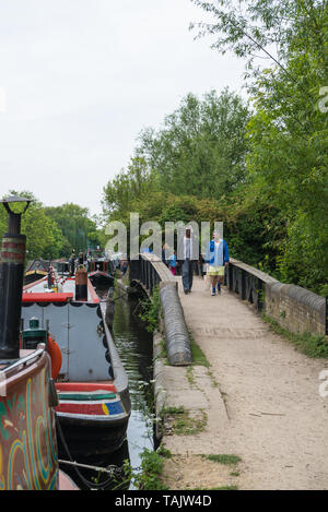 Zwei Männer, die über die kleine Brücke am Grand Union Canal Treidelpfad. Schmale Boote, die in der Jährlichen Rickmansworth Festival sind entlang des Kanals vertäut. Stockfoto