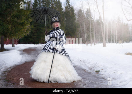 Ältere Frau in einem gothic Kleid in einem Hut mit einem schwarzen Dach auf die Natur im Winter Stockfoto