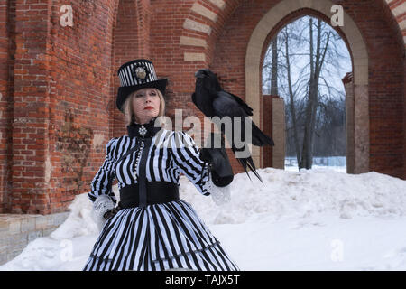 Eine ältere Frau in einem Kleid mit einem schwarzen Raben hat auf die Natur im Winter Stockfoto