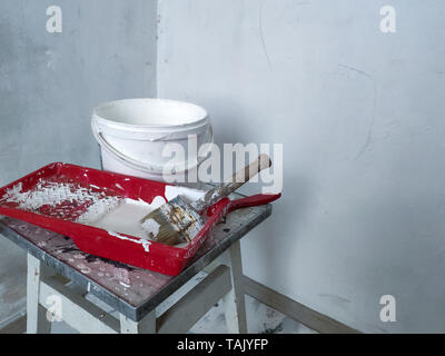 Closeup of a red tray with white paint and brushes and a paint bucket over the light walls, concept of renewing life and repair Stockfoto