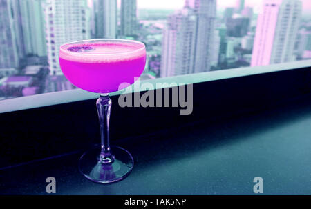 Shocking pink Cocktail auf die Tabelle, in der sich die Bar auf der Dachterrasse mit Blick auf die Hochhäuser im Hintergrund Stockfoto