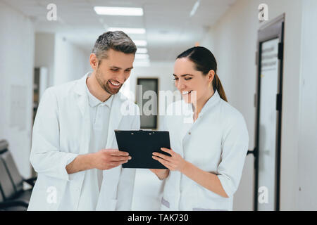 Zwei Ärzte, die über einen Fall steht am Krankenhaus Flur. Teamarbeit und Kommunikation medizinische Personal Stockfoto