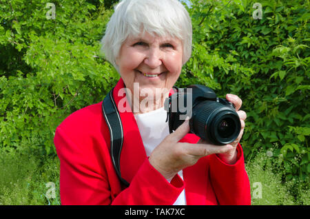 Portrait von Lächeln, glücklich Großmutter genießen Sie Ihr Hobby bei Sun Tag. Moderne kaukasischen Granny ist professioneller Fotograf. photocamera in der Hand der alten Dame. Rentner Technologie verwenden Stockfoto