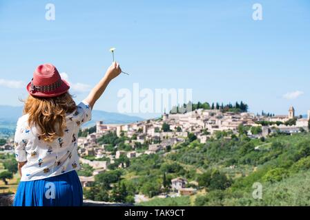 Spello, Perugia, Umbrien, Italien. Panorama der Stadt der Blumen, im grünen Herzen von Italien. Von hinten ein Mädchen in einem Red Hat mit einer Blume. Stockfoto