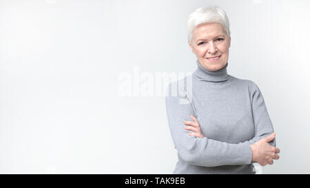 Zuversichtlich lächelnd Schöne gealterte Frau auf hellen Hintergrund Stockfoto