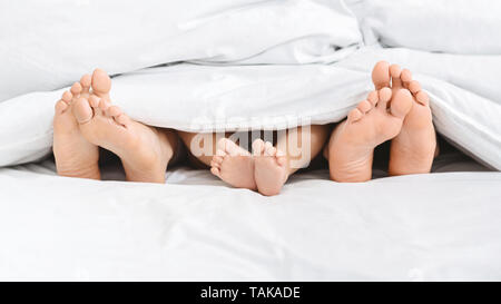 Drei Paar Füße von Happy Family im Bett Stockfoto