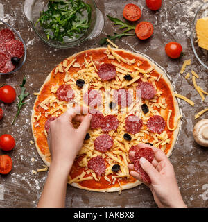 Koch Verzieren Pizza mit schwarzen Oliven und Salami Stockfoto