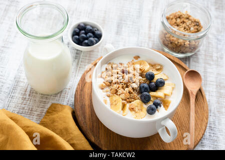 Müsli Schüssel mit Milch, Bananen- und Heidelbeeren auf weissem Holztisch Hintergrund. Konzept der gesunden Frühstück, gesund leben, Diät, Gewichtsverlust Stockfoto