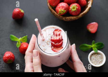 Strawberry Smoothie oder Milchshake in Glas auf schwarzem Hintergrund. Hände halten kalt Erfrischende Sommer trinken. Gesunde Ernährung Konzept Stockfoto
