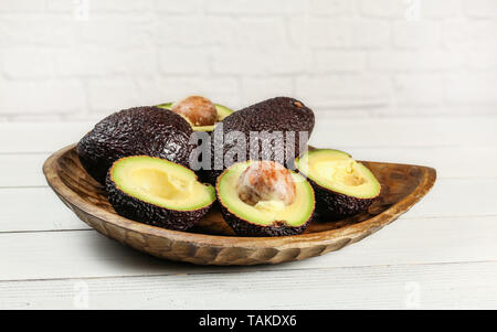 Braun Avocado reif, bilse Sorte, halbiert sich auch die ganzen Birnen, aus Holz geschnitzte Schale und Tafeln Schreibtisch Stockfoto