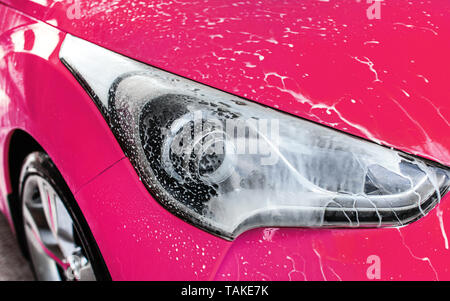 Rosa Auto vorne Licht im selbst gewaschen dienen Carwash, weiß Shampoo Schaum fließt auf Glas Stockfoto