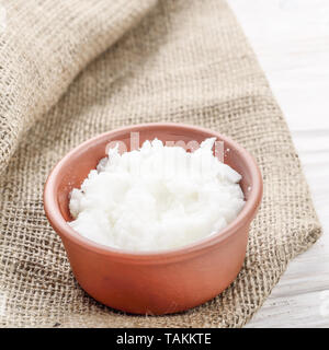 Kokosöl in braun Ton Schüssel auf Hanf Sack auf weißen Küche aus Holz Tisch Stockfoto