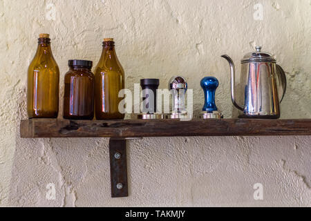 Kaffee Tamper und Schwanenhals Wasserkocher auf Anzeige auf einem Holzregal auf einen Kaffee Wand hacken. Stockfoto