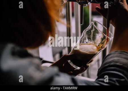 Mädchen gießt ein Pint Bier in einem Handwerk Bier Pub. Örtlichen Pub. Glänzend Bier Tippen auf den Hintergrund. Die hellen sonnigen Nachmittag. Von einer Schulter schauen Stockfoto