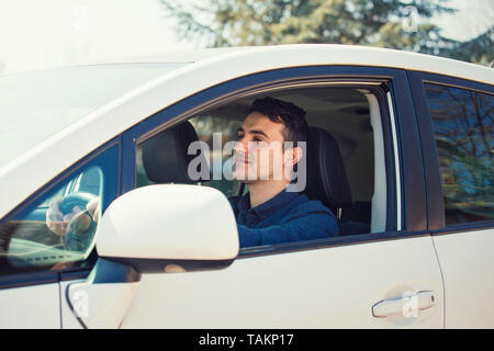 Erfolgreiche junge Mann, der sein neues weißes Auto hält Hand am Lenkrad nach vorn glücklich ein sicheres Gefühl. Zuversichtlich, Geschäftsmann, Lächeln, Genießen Stockfoto