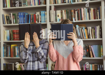 Junge Frauen ausblenden Gesichter hinter Bücher in der Bibliothek Stockfoto