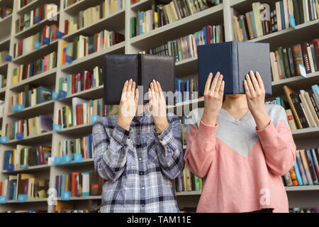 Junge Frauen ausblenden Gesichter hinter Bücher in der Bibliothek Stockfoto