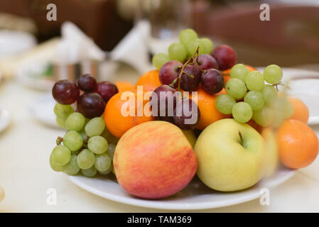 Früchte und Beeren auf Urlaub. Trauben, Äpfel, Mandarinen auf Tellern auf den Tisch. Stockfoto