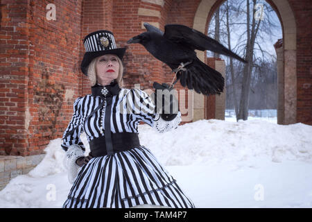 Eine ältere Frau in einem Kleid mit einem schwarzen Raben hat auf die Natur im Winter Stockfoto