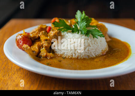 Curry Huhn helle saftig mit weißer Reis auf dem Teller über Holz- Hintergrund. Von der Seite. Foto Stockfoto