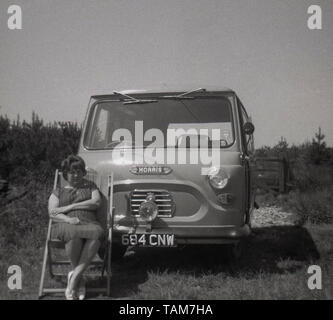 1960, historische, oh die einfachen Freuden des Lebens.... eine Frau sitzt im Liegestuhl an der Vorderseite eines Morris Commerical J4 Van in einem Feld geparkt, England, Großbritannien Stockfoto