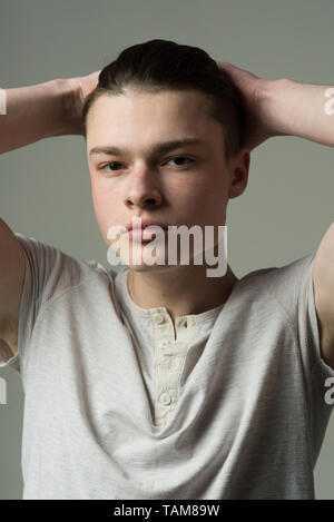 Kerl auf zuversichtlich Gesicht in Light shirt berührt Haar, grauen Hintergrund. Macho mit stilvollen lange Haare schneiden. Friseur- und Frisur Konzept. Glatter Mann Stockfoto